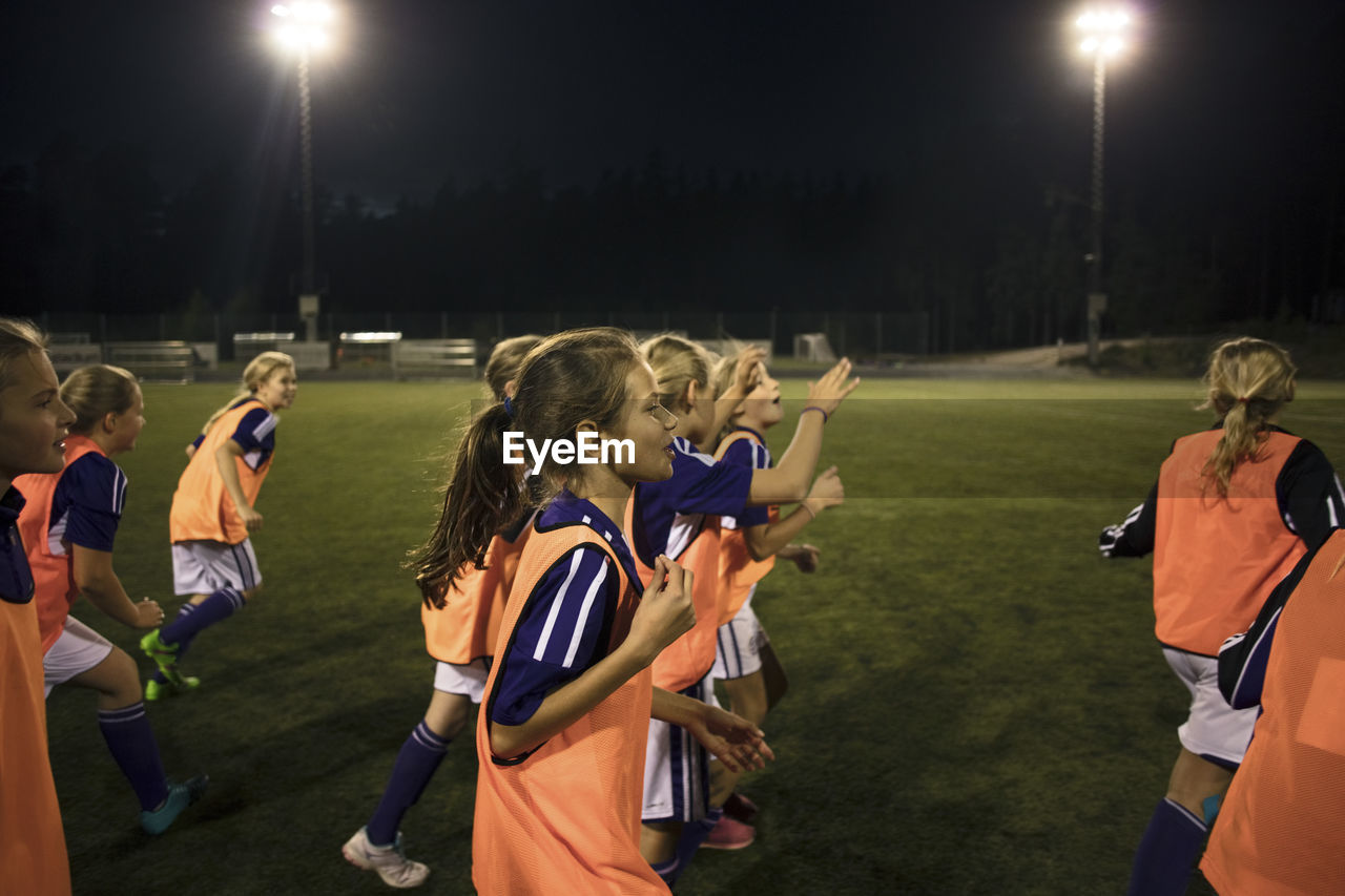 Girls running on illuminated soccer field at night