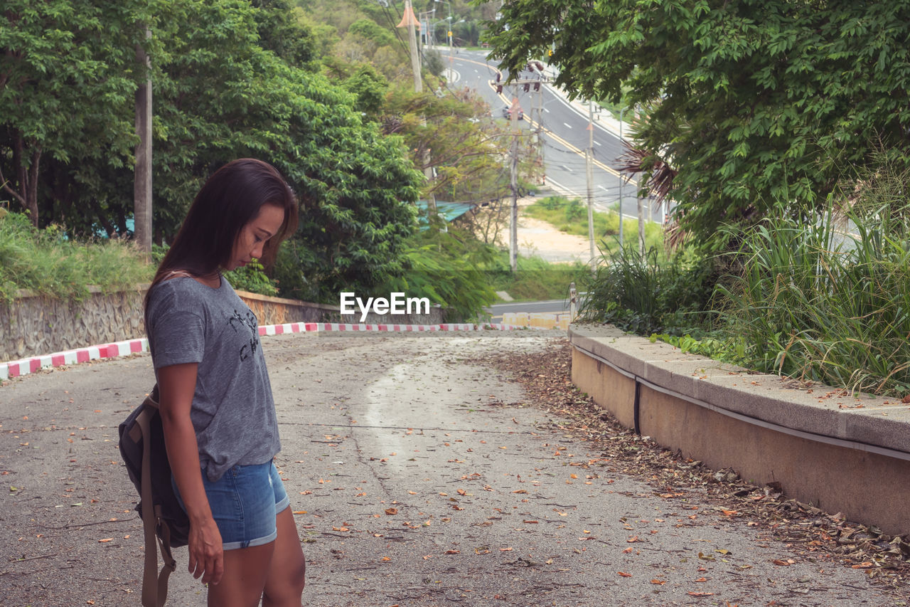 Side view of young woman standing against trees