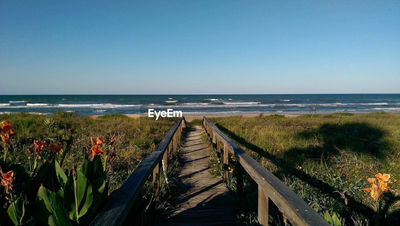 Walkway leading towards beach against clear blue sky