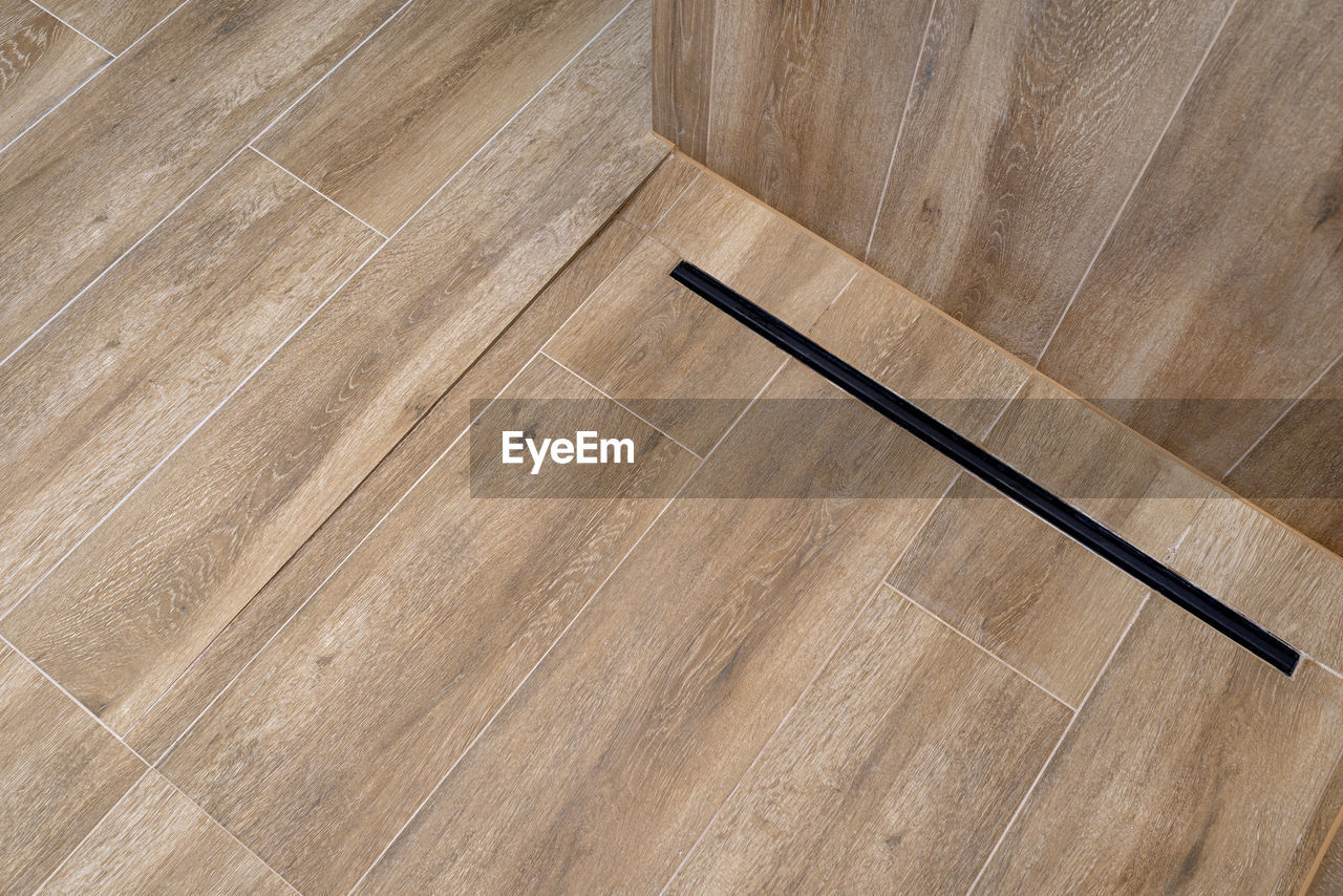 Modern black linear drain in a bathroom lined with ceramic tiles imitating wood.