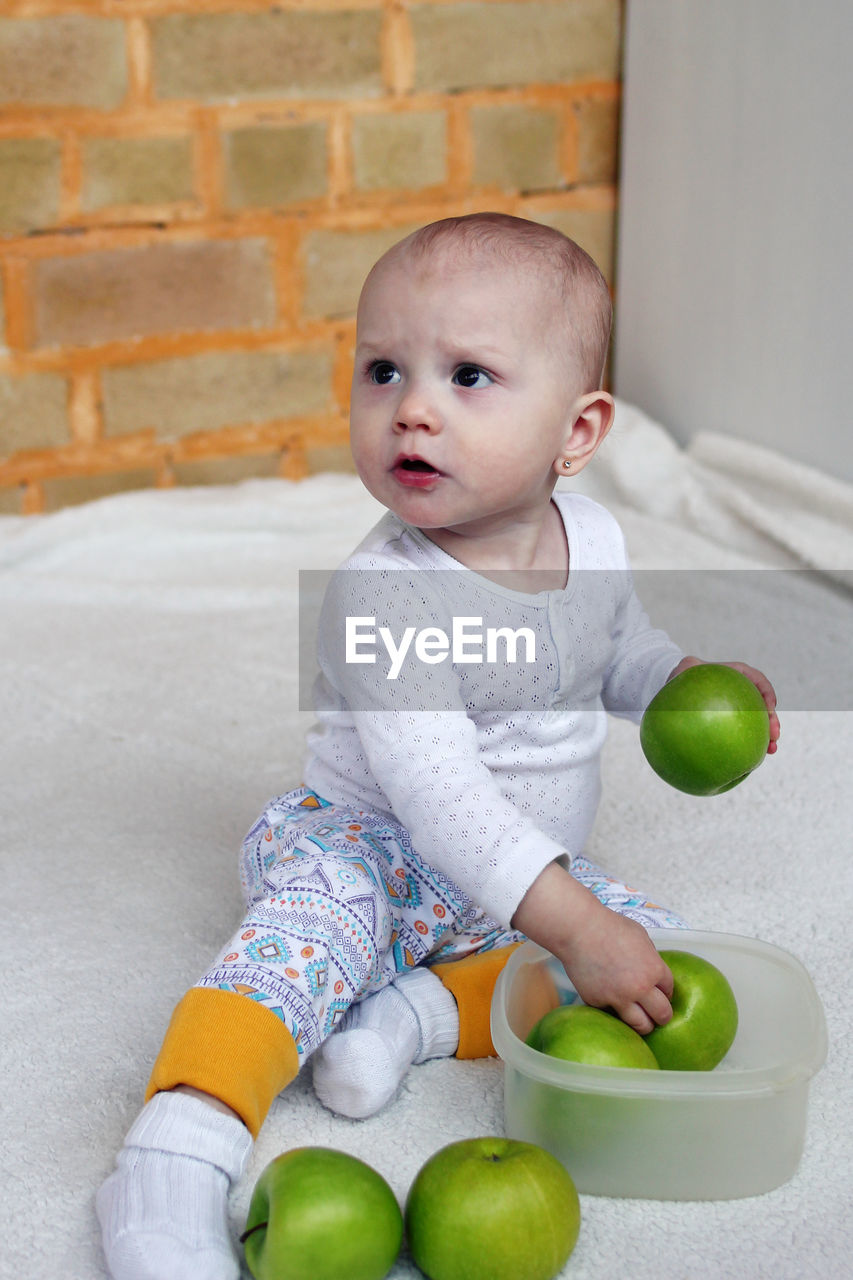 High angle view of cute baby girl sitting on carpet with apple at home