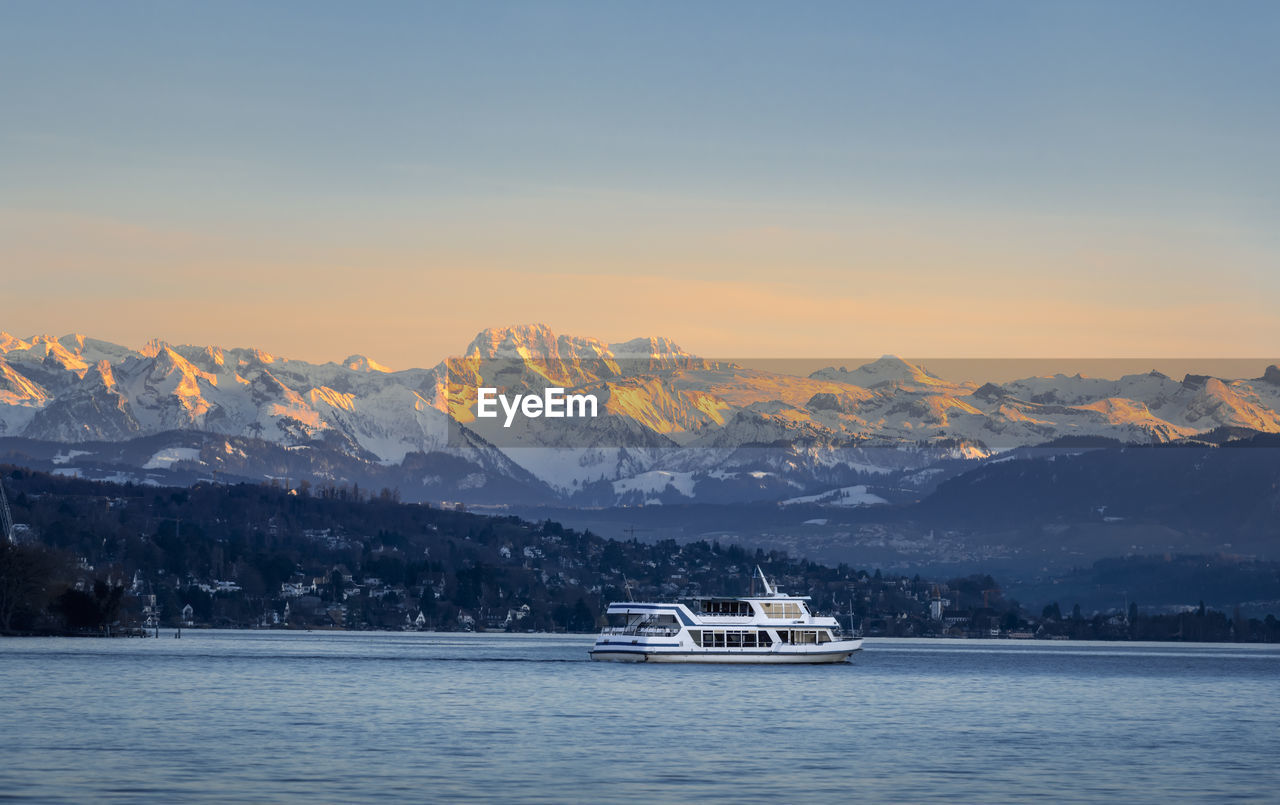 Scenic view of snowcapped mountains by sea against sky during sunset