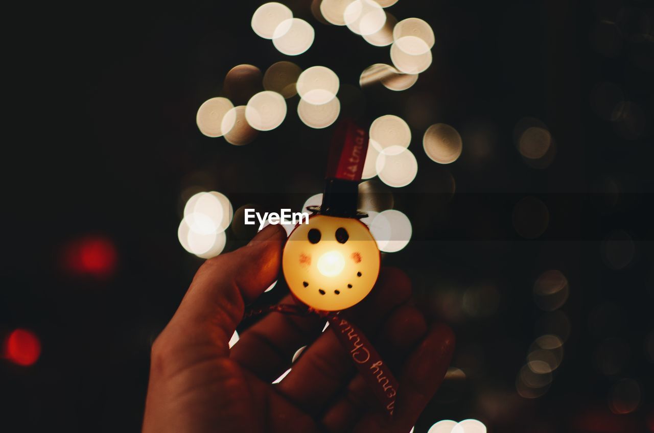 Cropped image of person holding illuminated christmas ornament at night