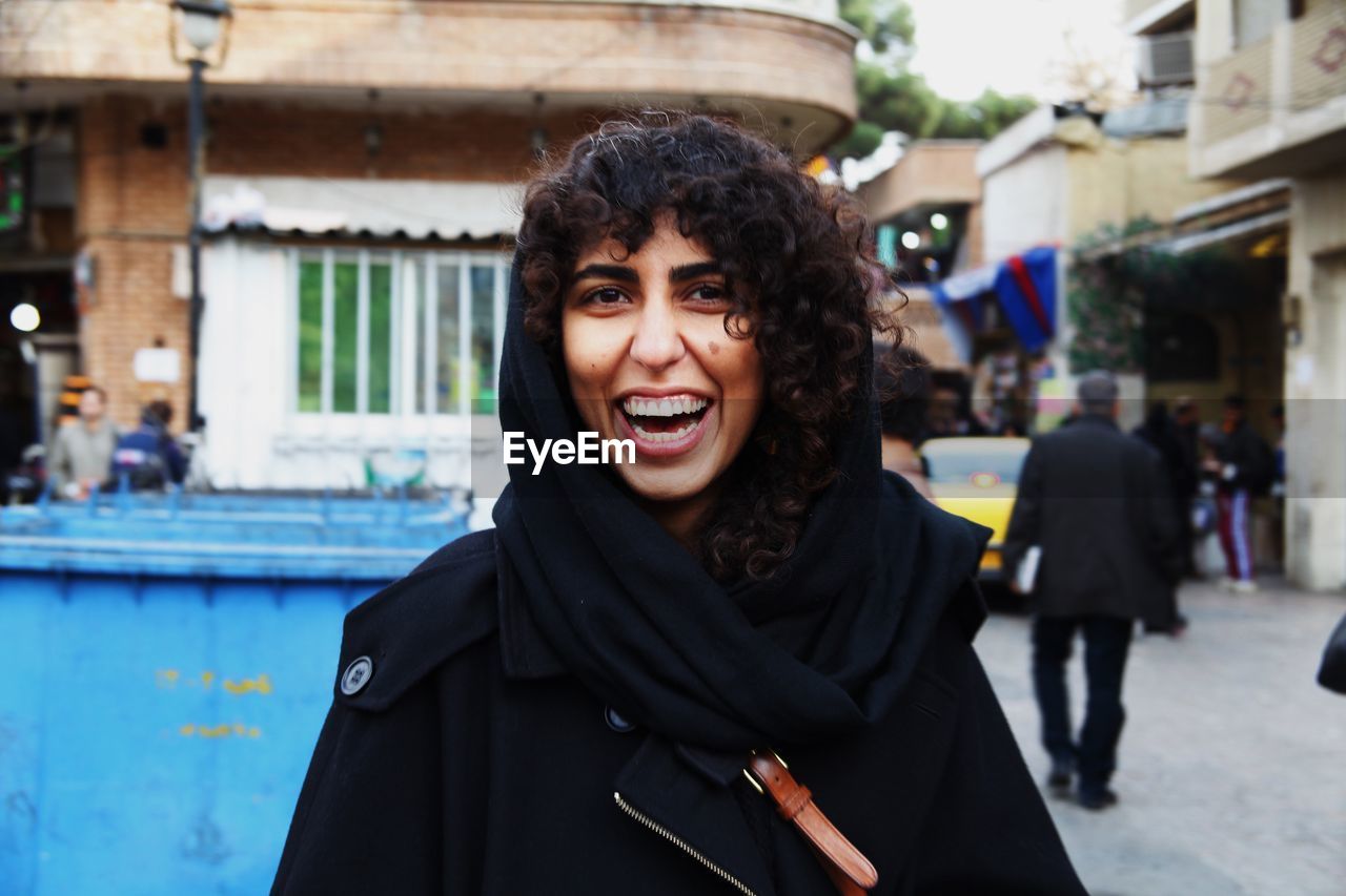 Portrait of happy woman standing against buildings in city