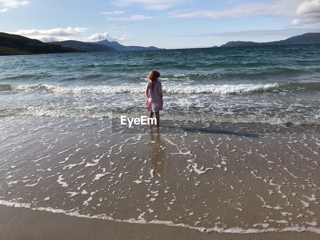 Rear view of girl standing on beach against sky