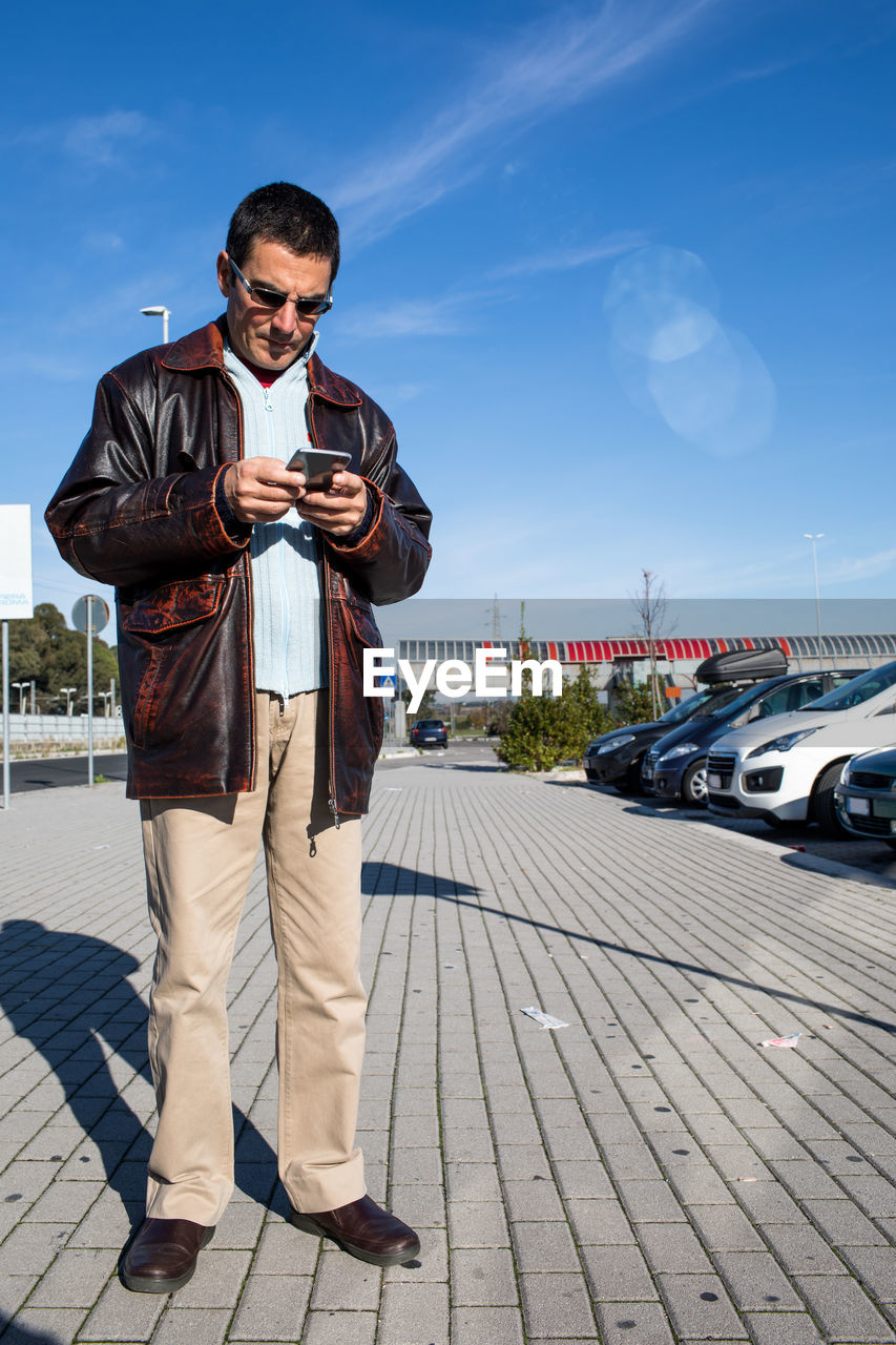 FULL LENGTH OF YOUNG MAN STANDING ON SMART PHONE