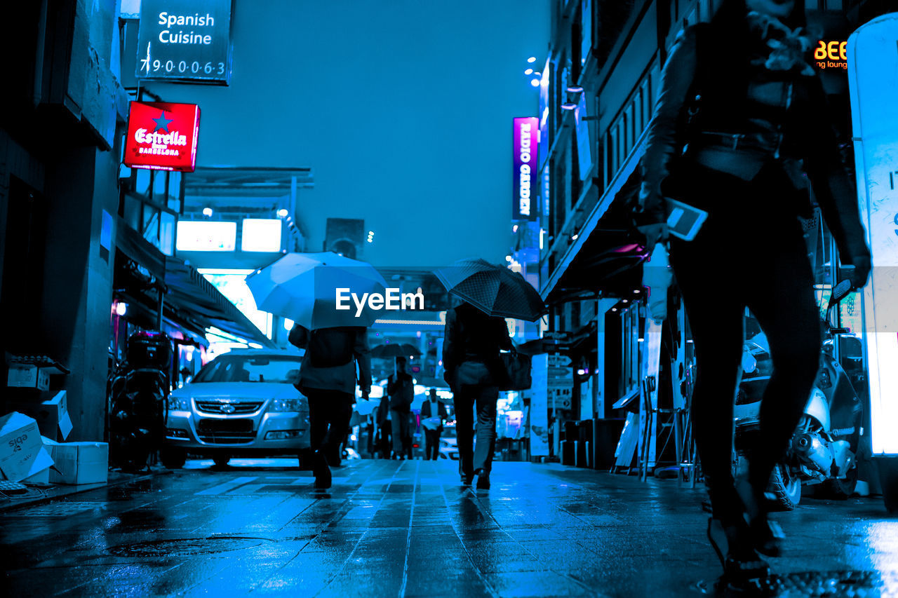 PEOPLE WALKING ON ILLUMINATED STREET IN CITY