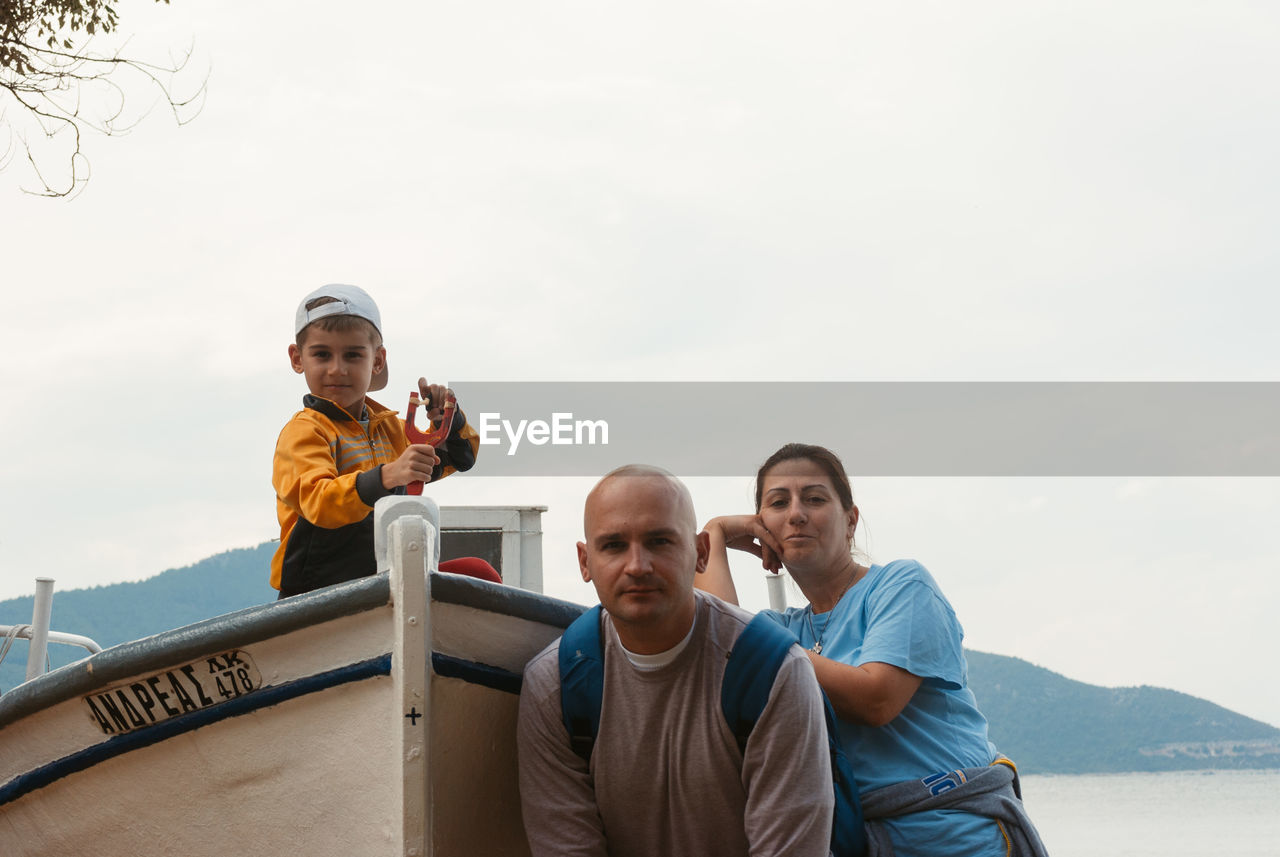 Portrait of father and mother with son in boat against clear sky at shore