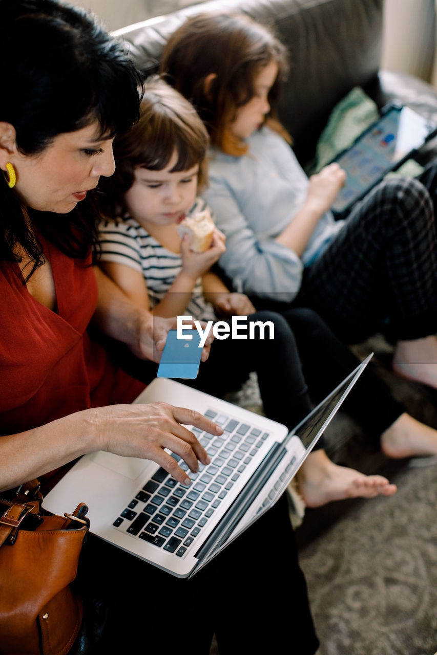 High angle view of woman doing online shopping through laptop while sitting with daughters at home