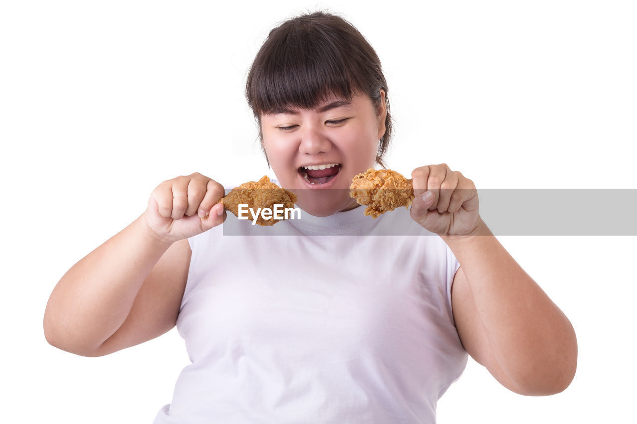 Young woman eating fried chicken meat against white background