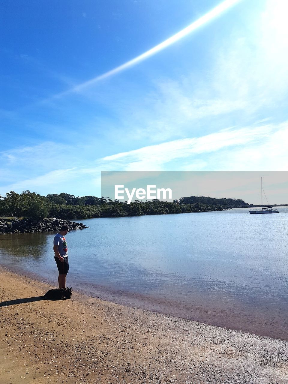 MAN SITTING ON SHORE AGAINST SKY