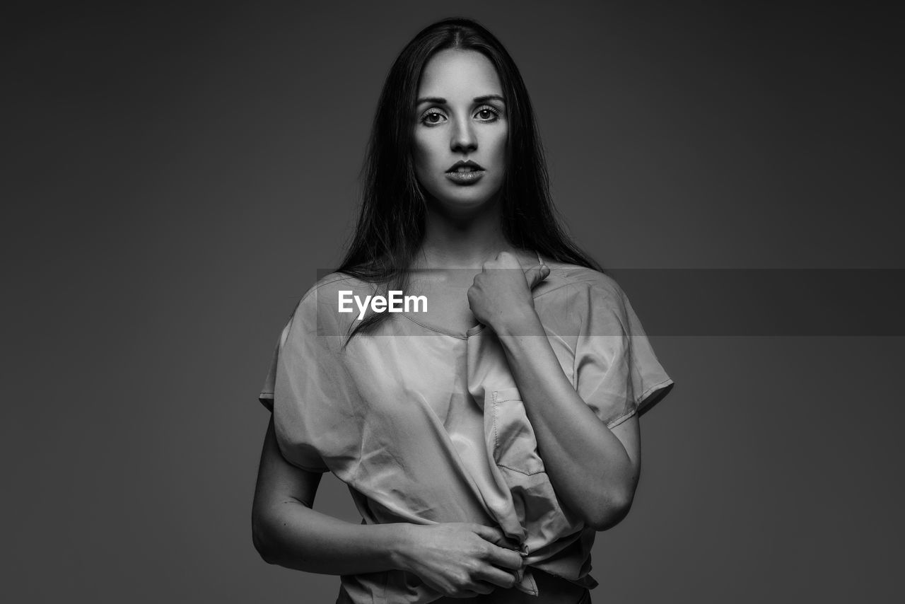 Portrait of woman holding top while standing against gray background