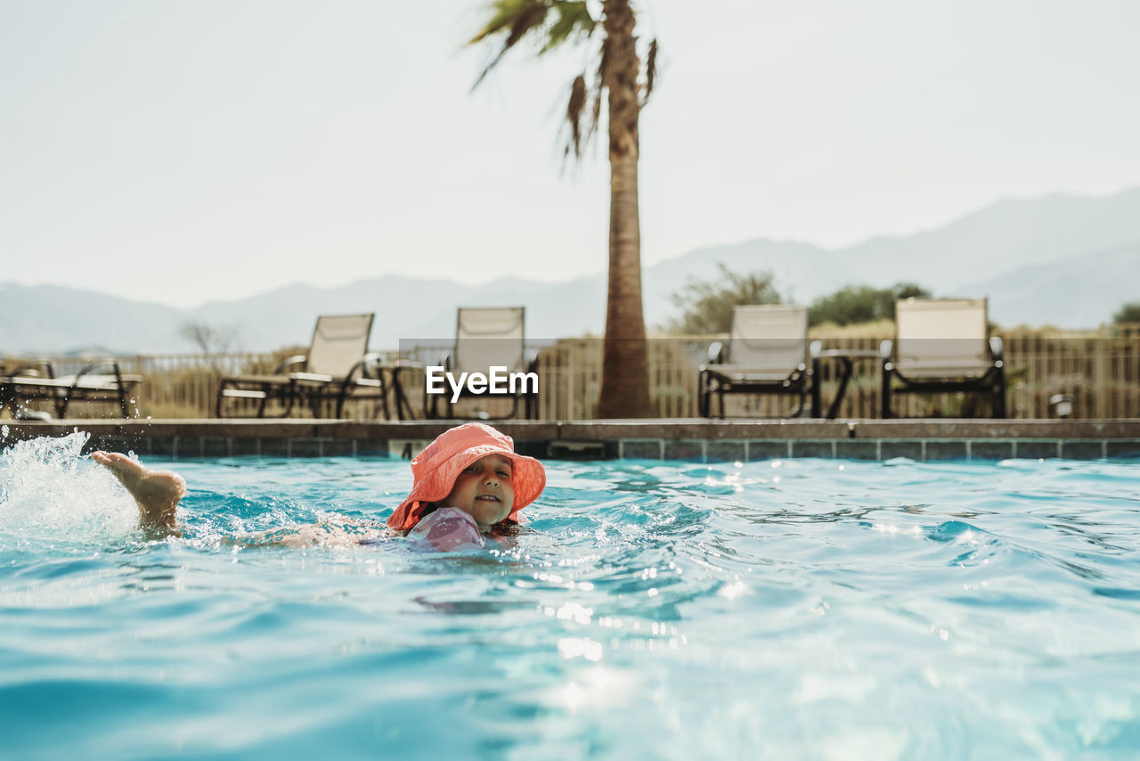 Side angle view of little girl in pink hat swimming in pool