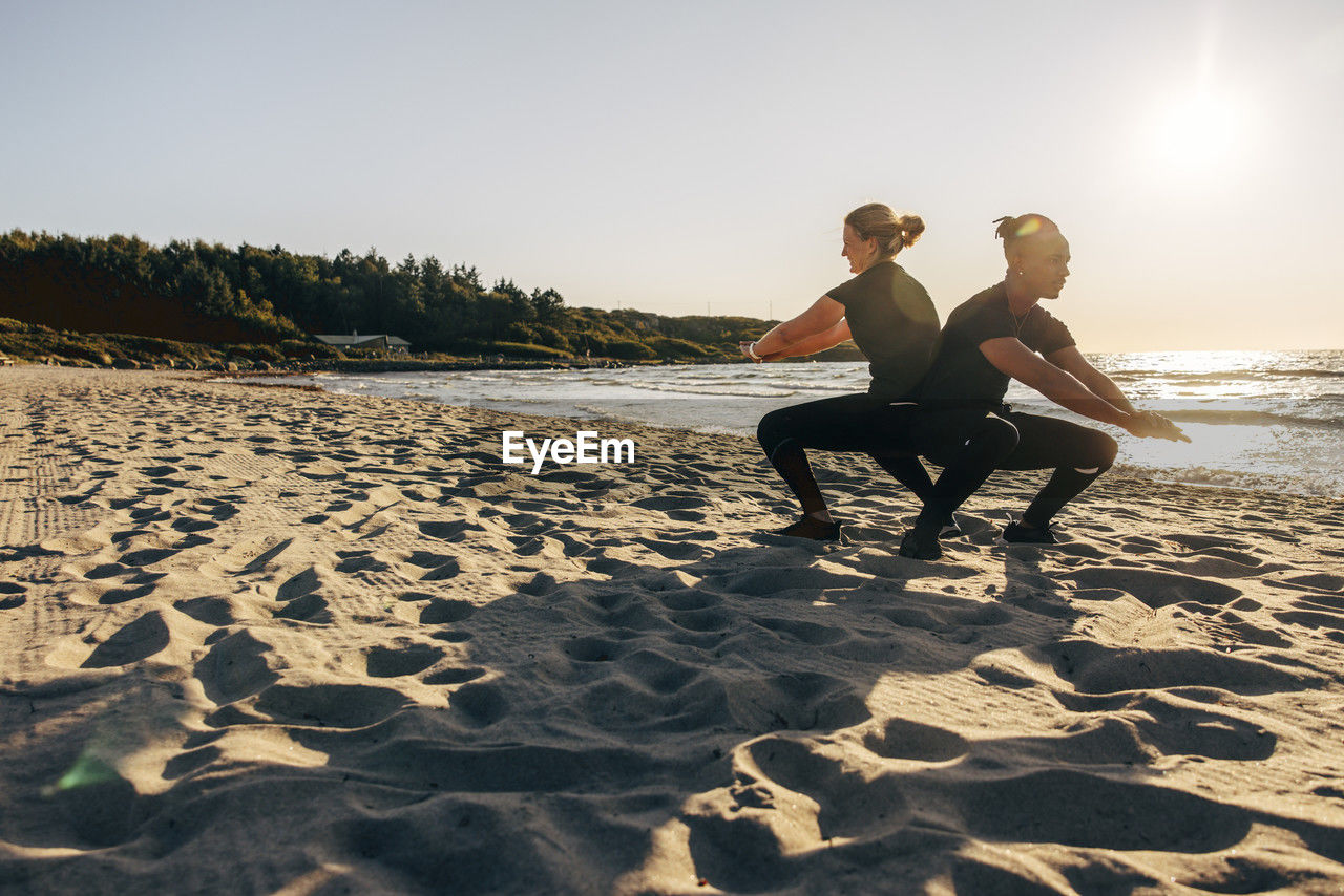 Man and woman practicing squats on sand at beach