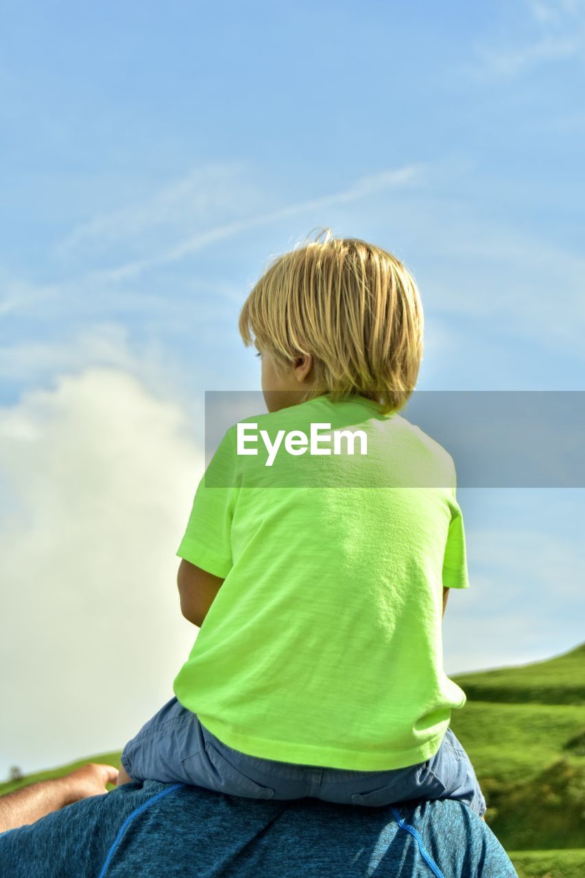 Rear view of boy sitting against sky