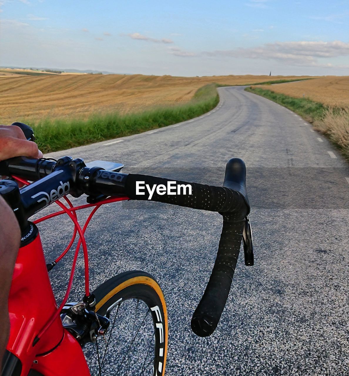 PERSON RIDING BICYCLE ON ROAD AGAINST SKY