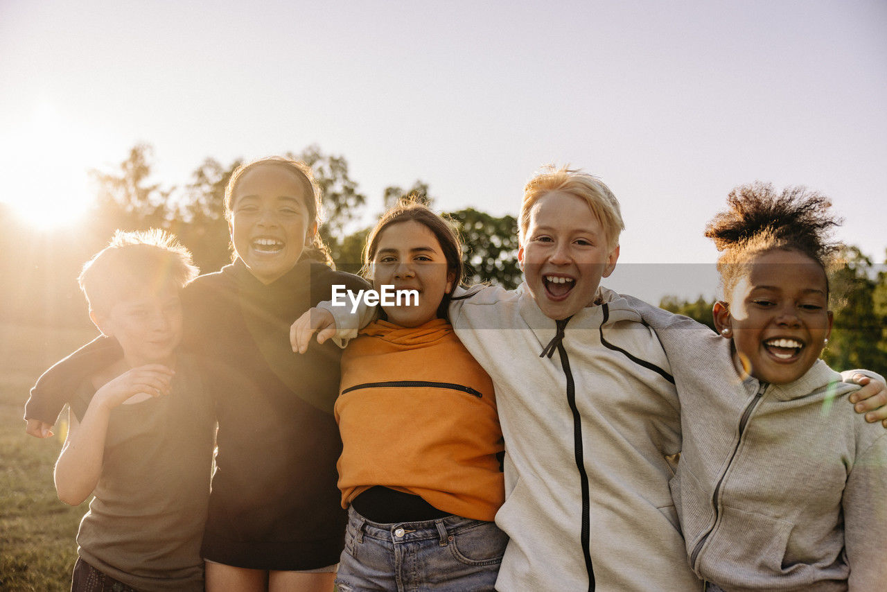 Portrait of cheerful kids with arms around playing together against sky