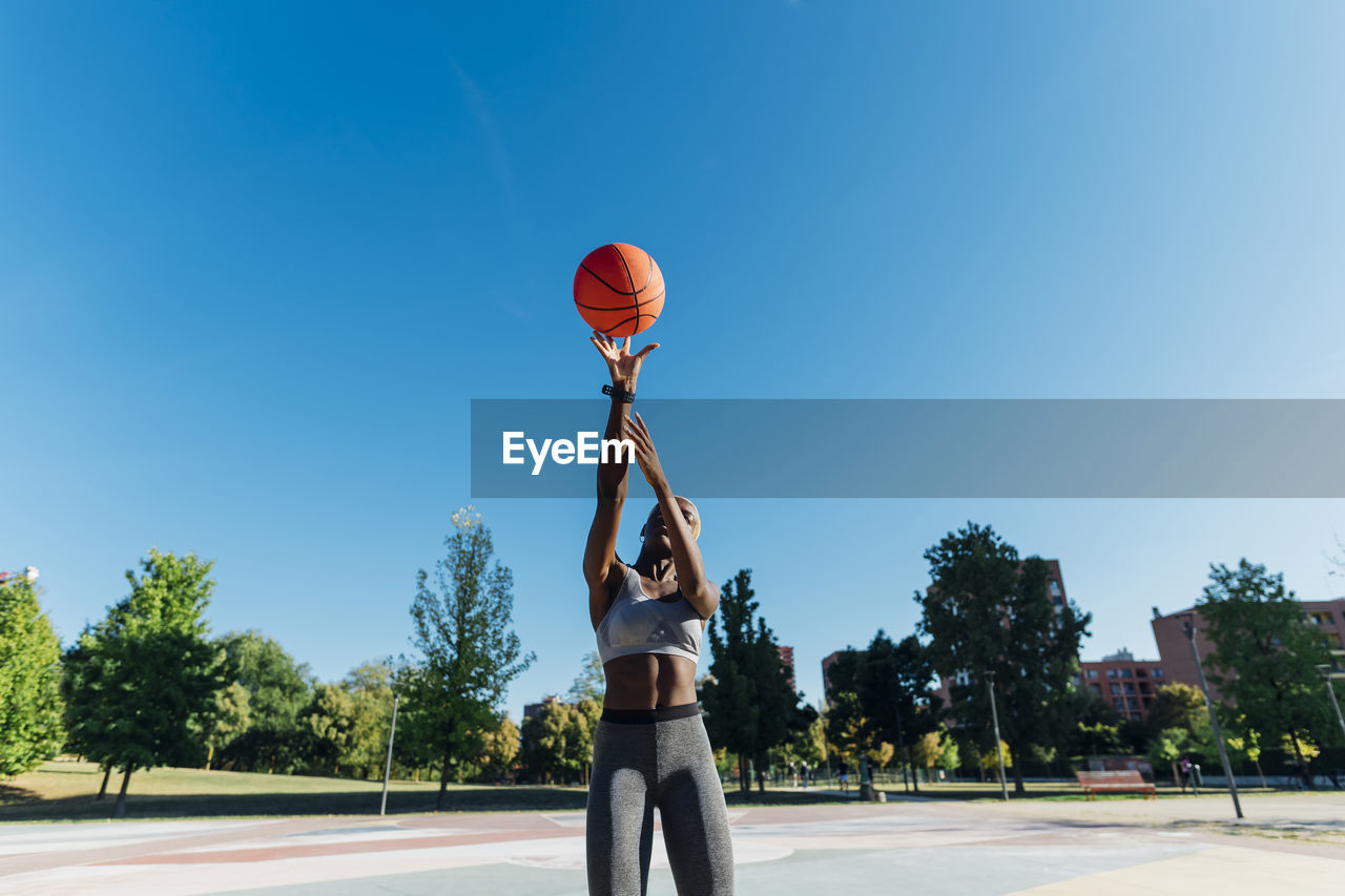 Basketball player throwing ball on sunny day