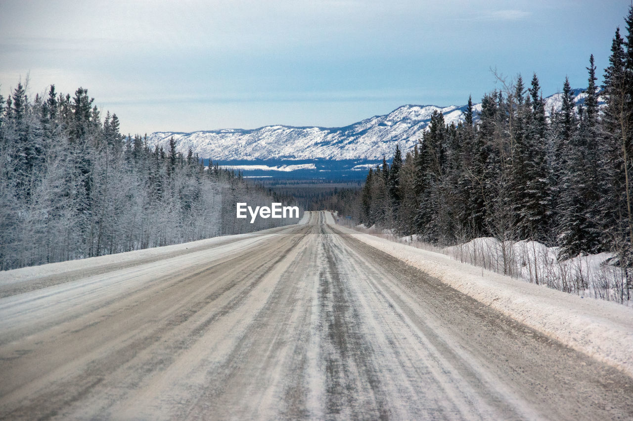 Snow covered road by mountain against sky