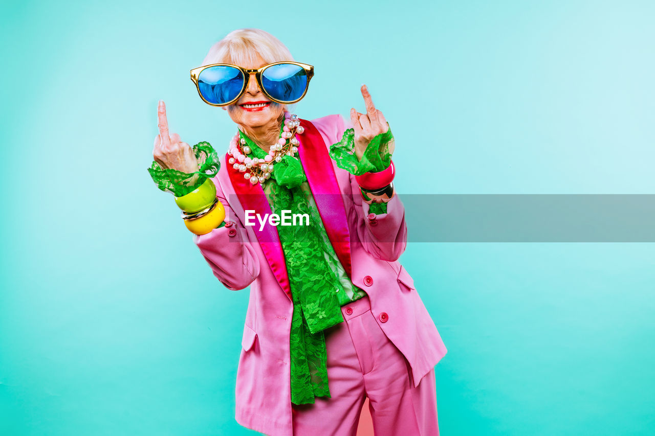 Portrait of senior woman wearing sunglasses gesturing against blue background