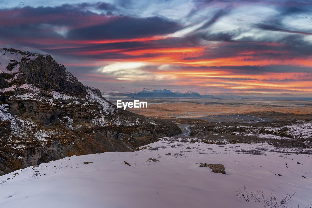 Scenic view of rocky cliffs on snow covered landscape against sky during sunset