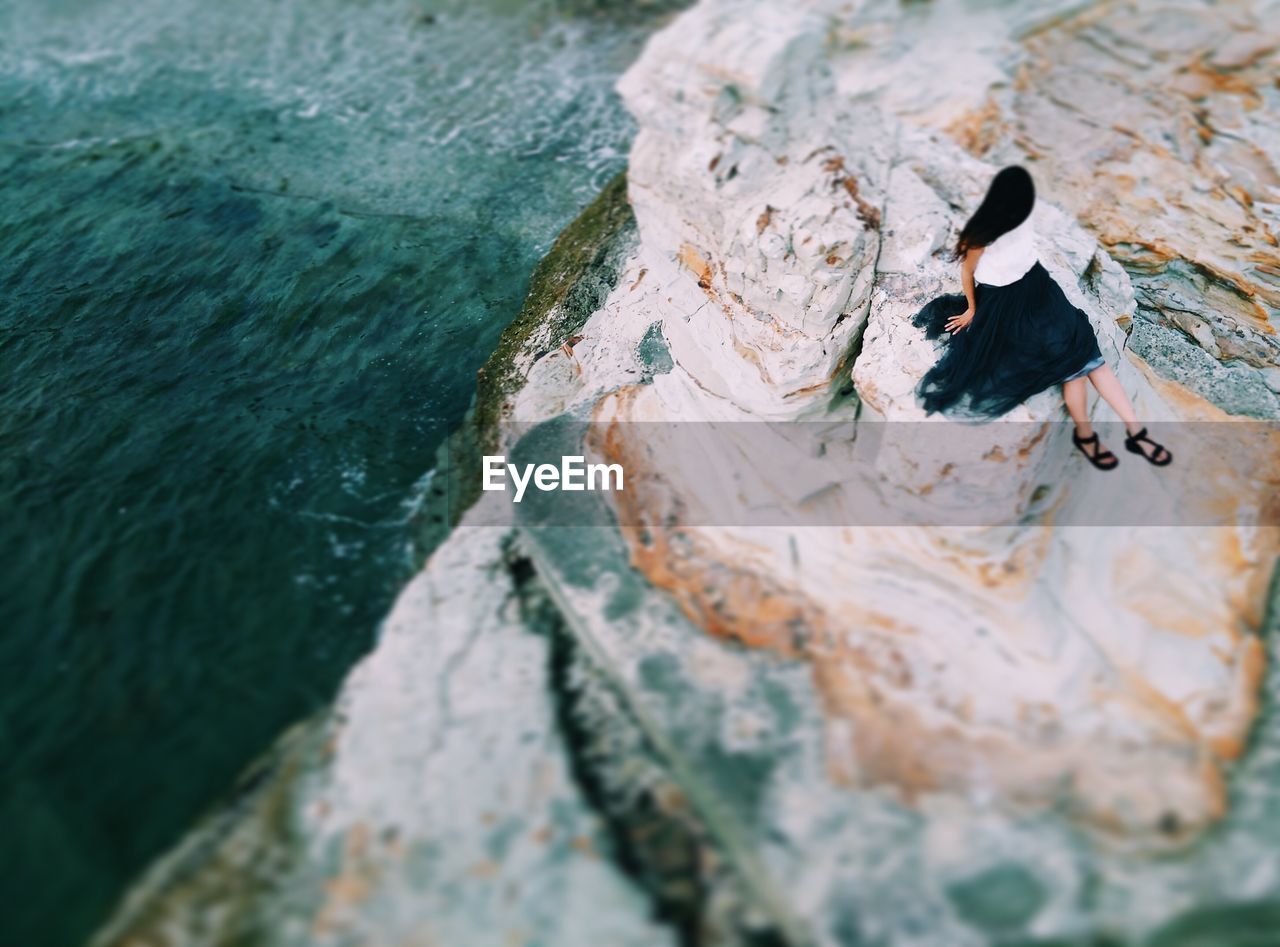 High angle view of woman sitting on mountain by sea