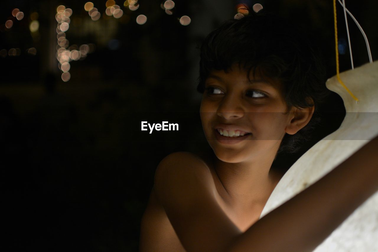 Smiling boy holding lighting equipment while standing outdoors at night