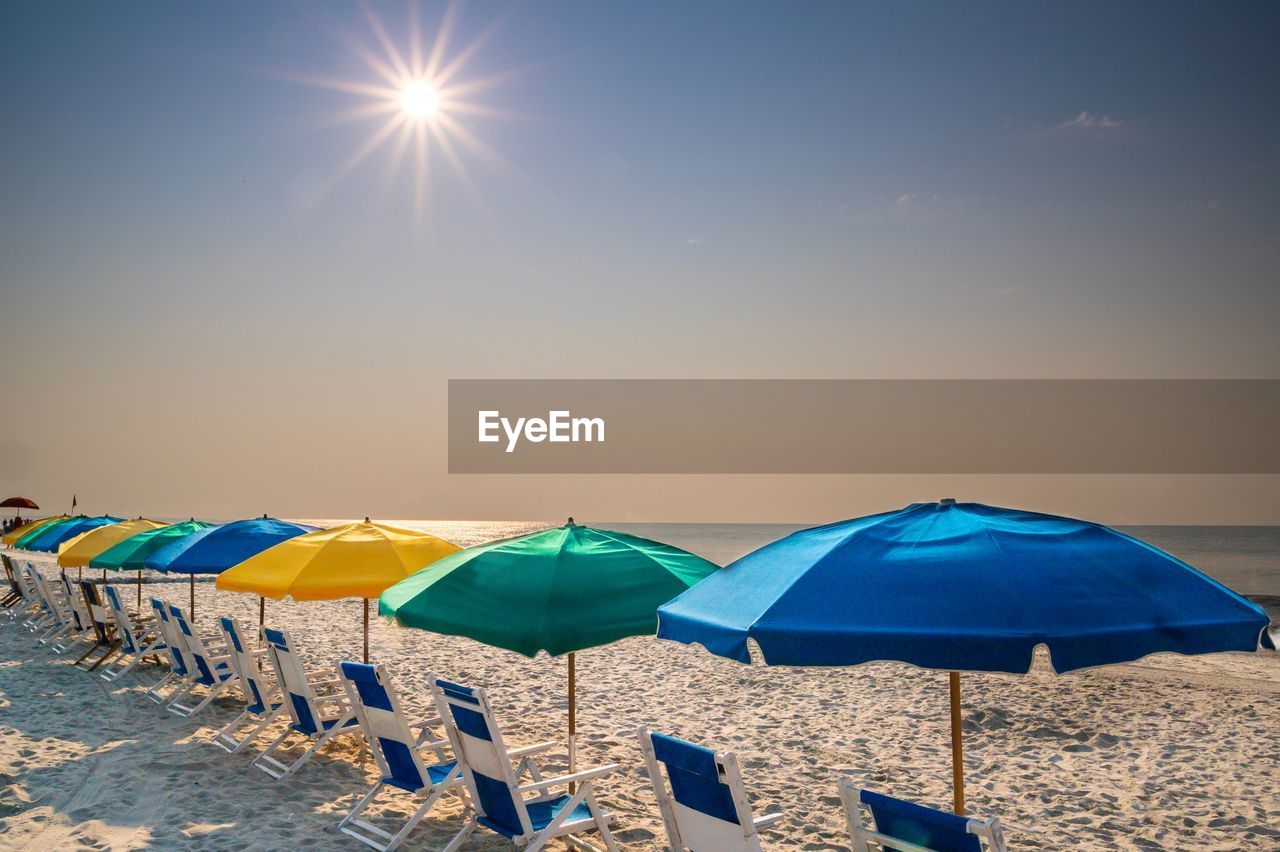 LOUNGE CHAIRS AND UMBRELLAS ON BEACH AGAINST BRIGHT SUN