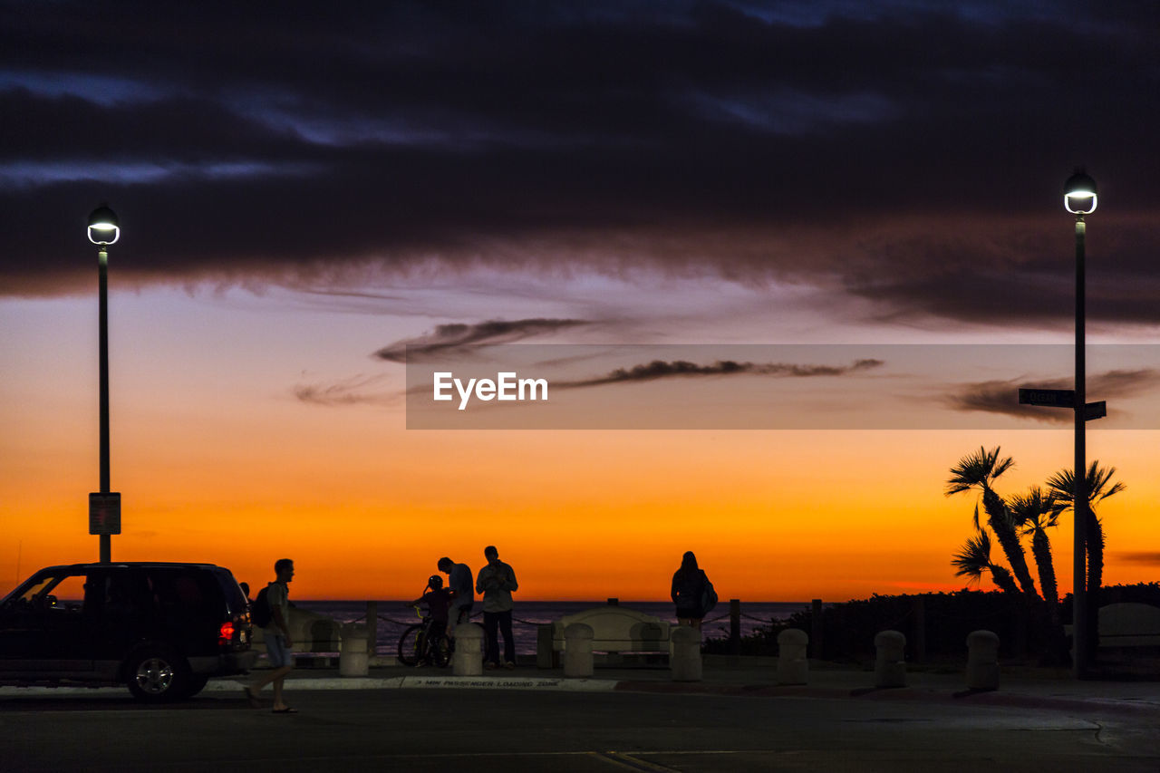 Silhouette people at beach against cloudy sky at sunset