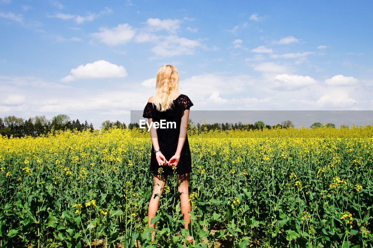 Rear view of woman with hands behind back standing on field