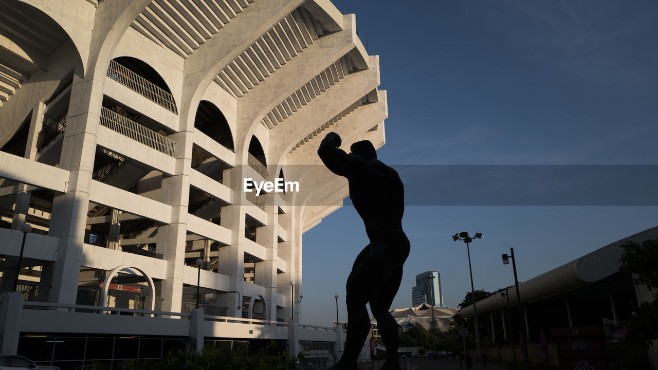 Low angle view of silhouette man statue standing against buildings in city