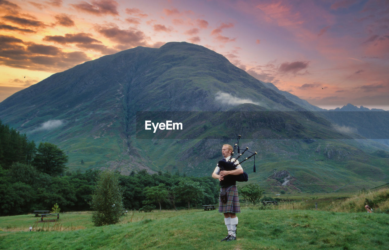 Full length of bagpiper standing on field against mountain