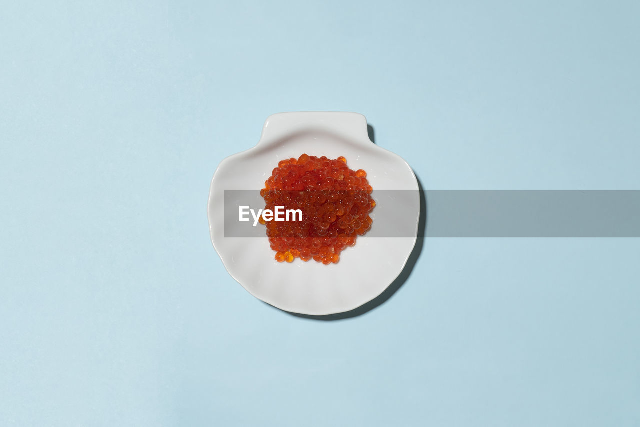 Porcelain plate with red caviar on a blue background.