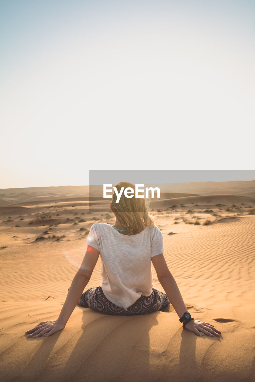 Rear view of woman sitting on sand at beach