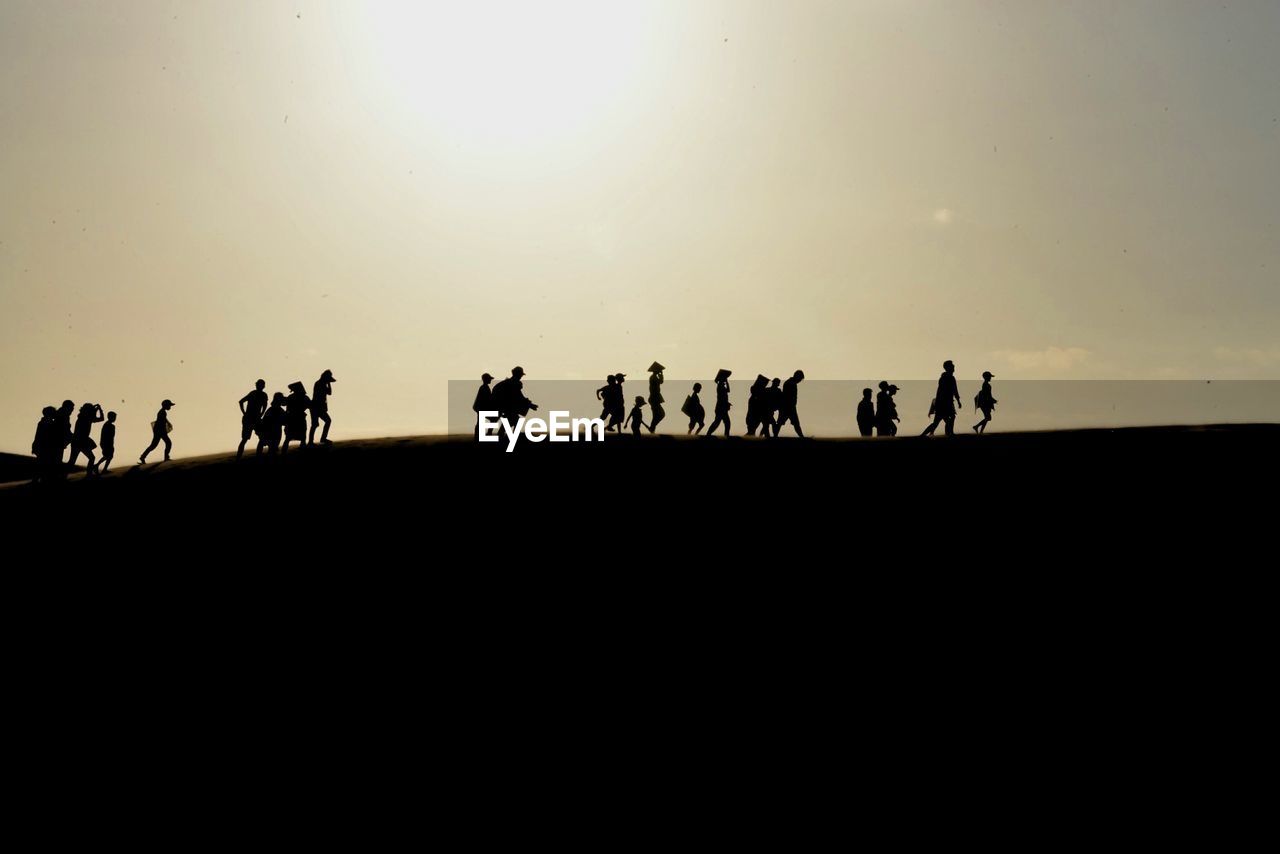 Low angle view of silhouette people walking in desert on sunny day