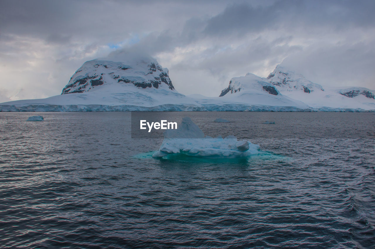 Iceberg in sea against cloudy sky