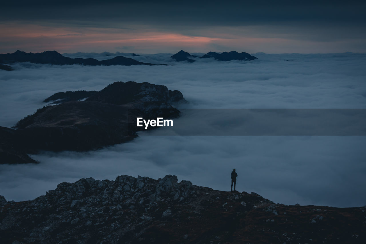 Man standing on rock against sky during sunset