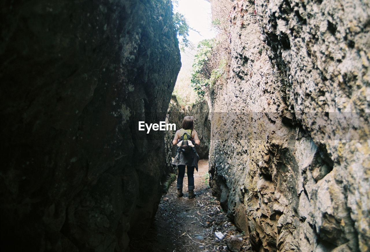 Full length rear view of woman walking on narrow alley amidst rock formations