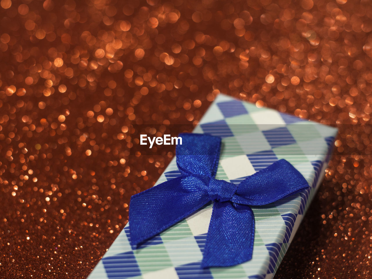 Close-up of christmas gift with blue ribbon on red glittering table