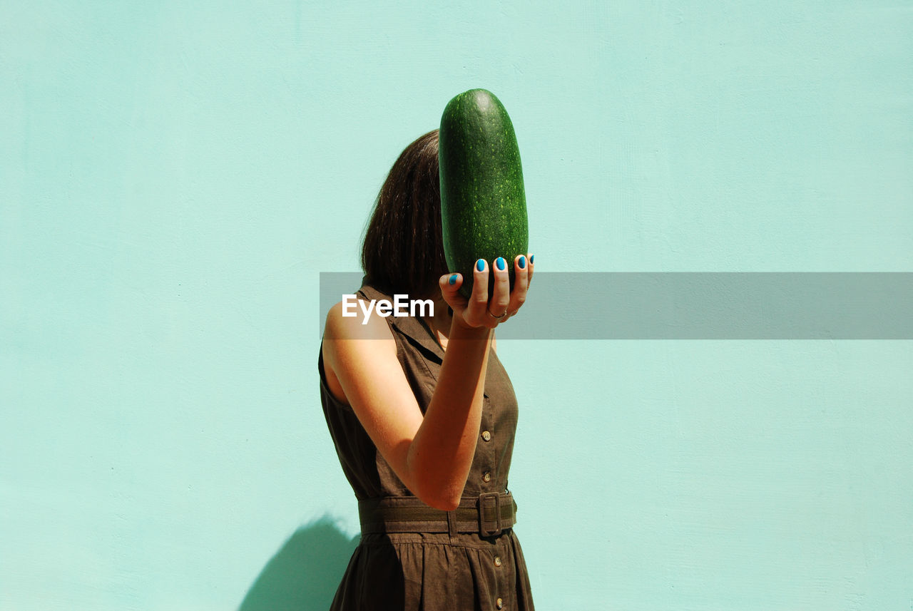 View of woman holding vegetable against wall