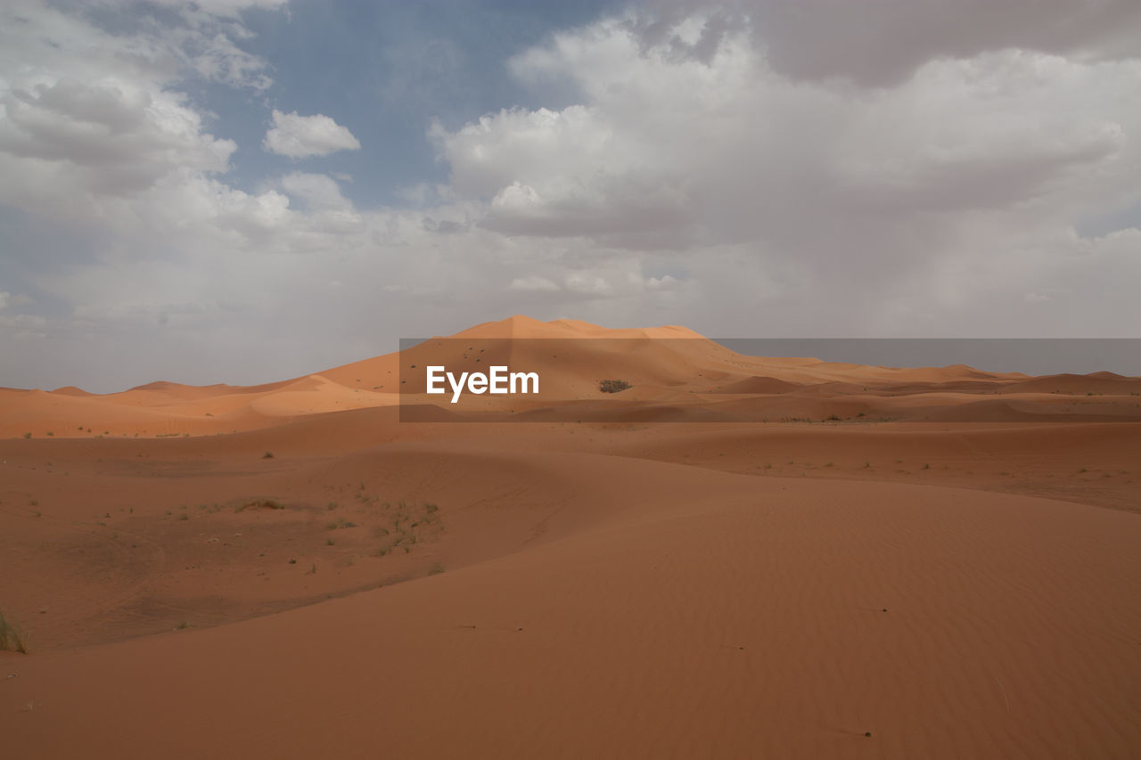 Sand dune in desert against cloudy sky