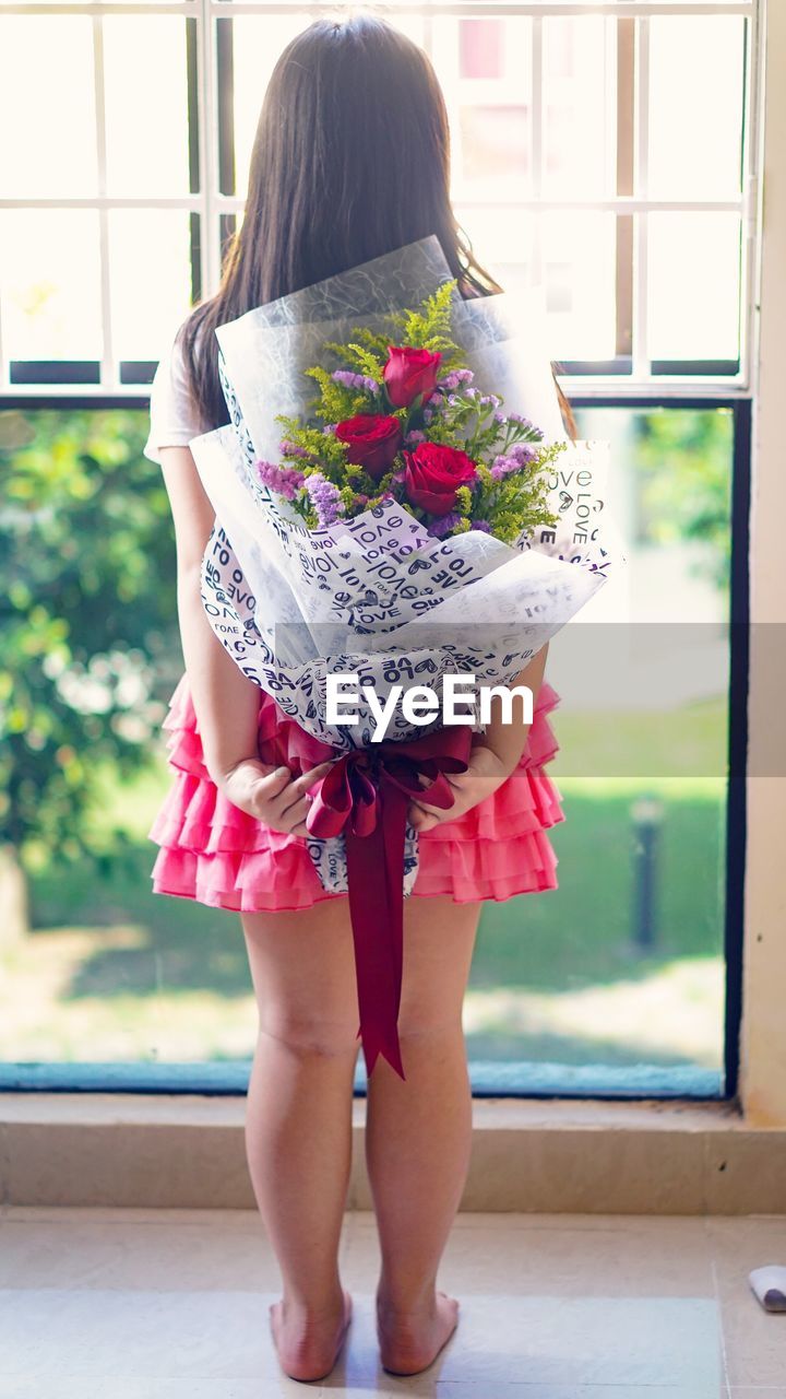 Rear view of girl holding bouquet at home