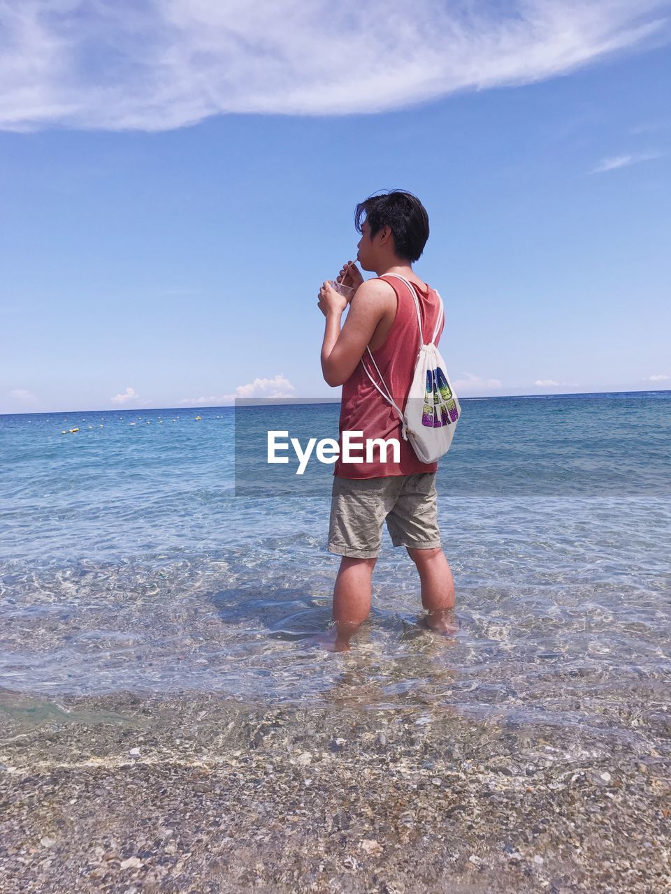 Man having drink while standing in sea against blue sky