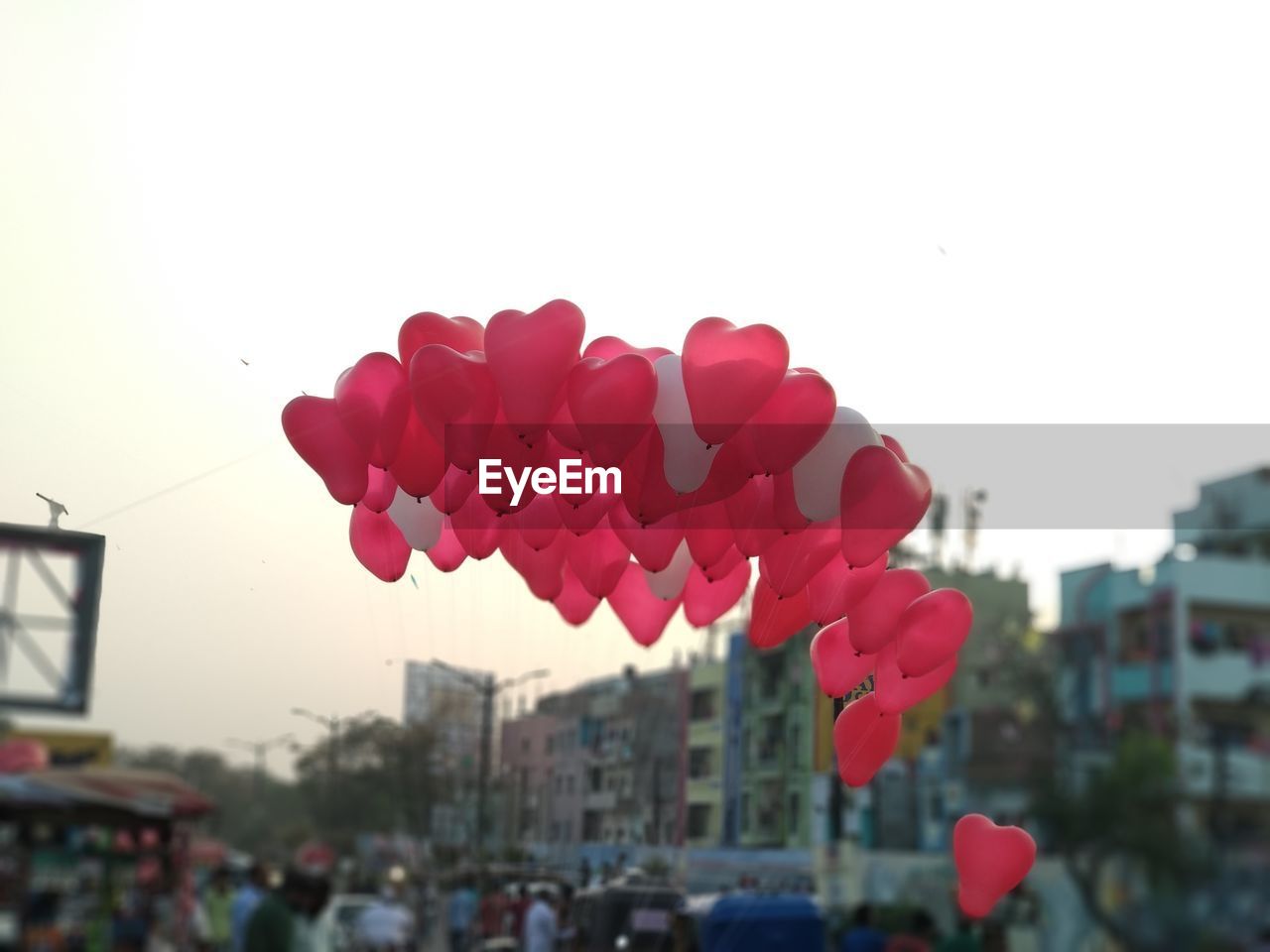 Low angle view of red heart shape balloons in city against clear sky