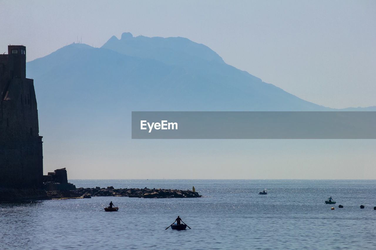 PEOPLE ON SEA BY MOUNTAIN AGAINST SKY