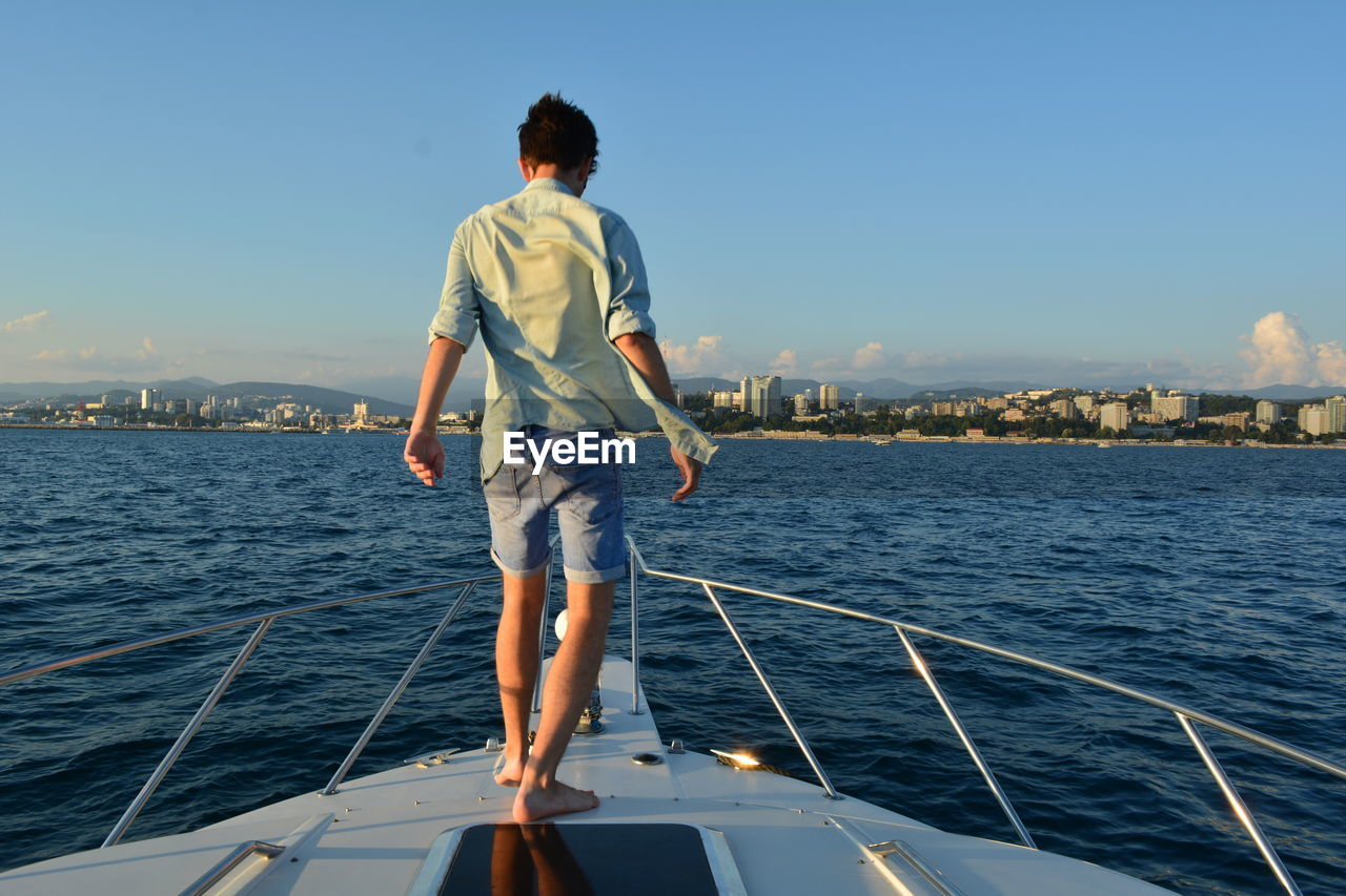 Rear view of young man on sailboat sailing in sea against sky