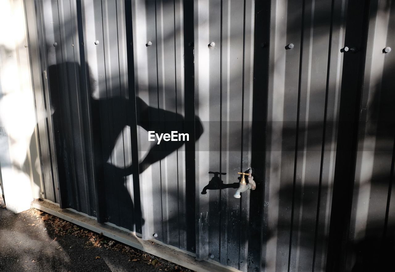 Tap on metallic fence with shadow of person