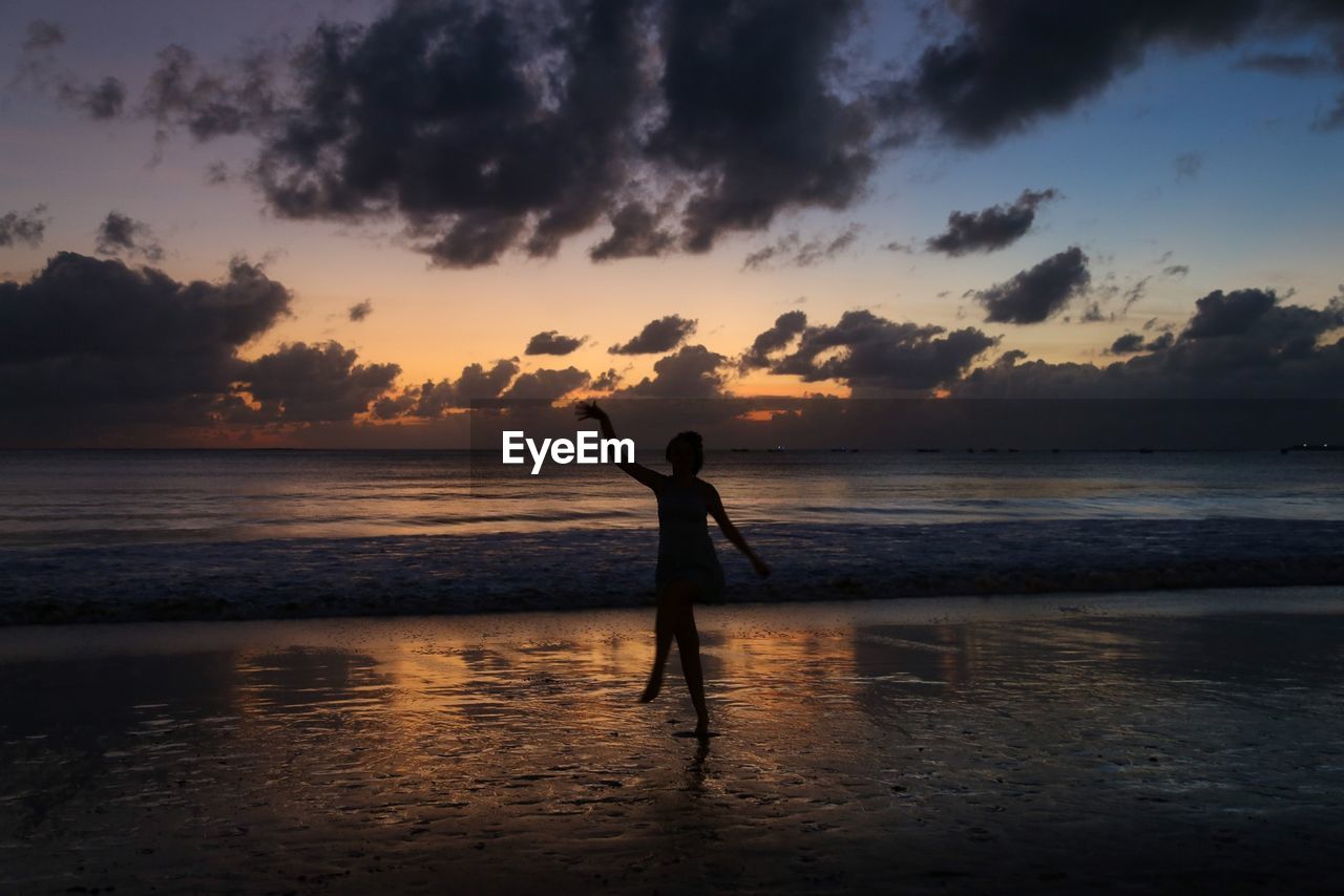 Silhouette woman dancing at beach against sky during sunset