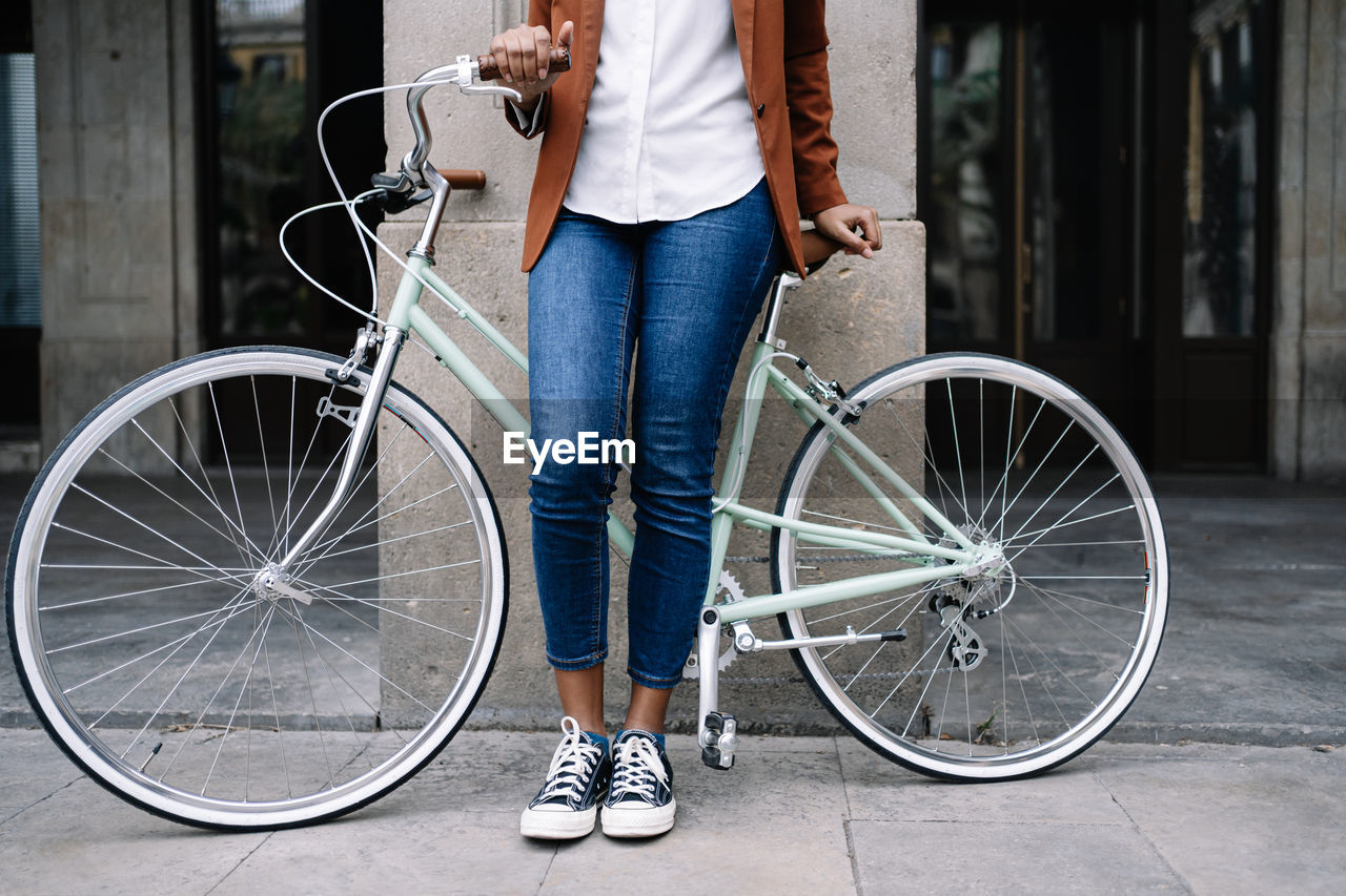 Crop black woman in smart casual style standing along street with bike