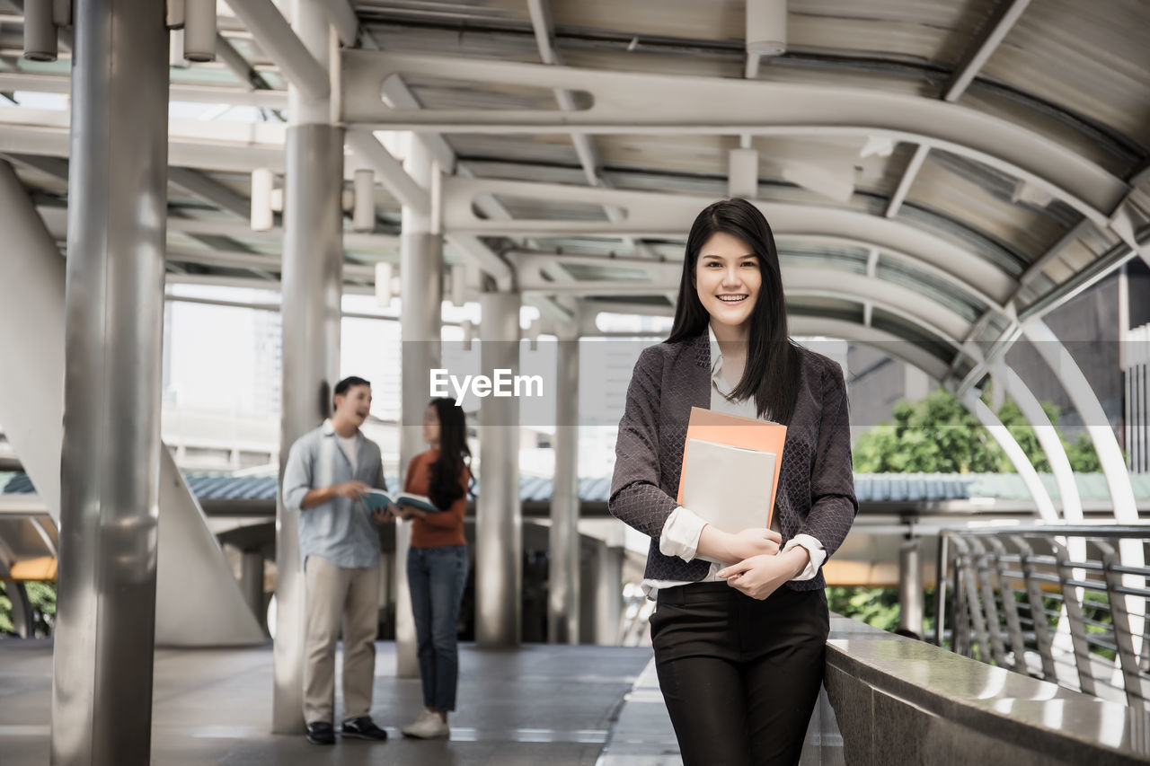 Portrait of woman holding book while standing by railing